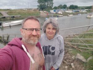 A man and a woman stand in front of a small river. The woman looks worried.