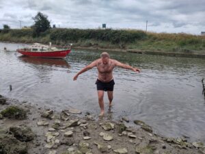 A man in swimming gear walks out of a narrow river