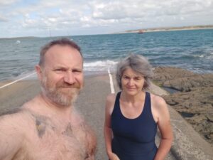 A man and a woman in swimgear stand on a slipway heading down into an estuary