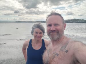 A man and a woman in swimming gear standing in front of an estuary