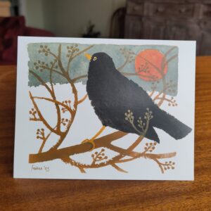 Christmas card with painted image of a blackbird on a branch against snow